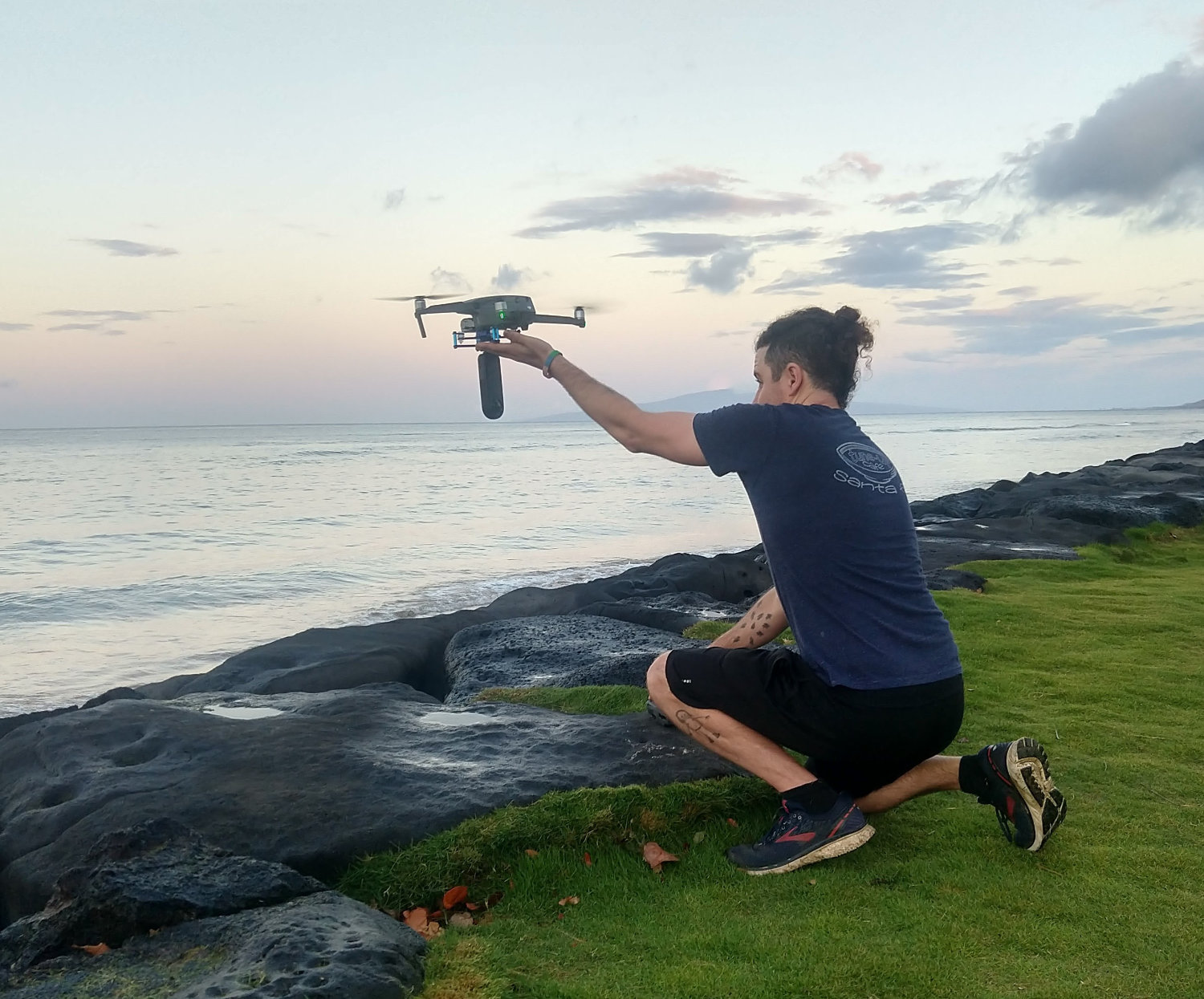 Drone pilot hand-catching DJI Mavic drone at ocean coastline during sunset